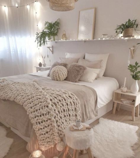 a white bedroom with lots of pillows and blankets on the bed, lights strung from above