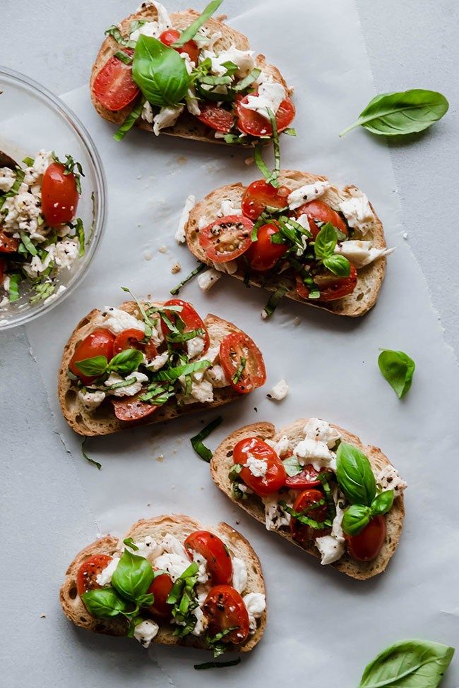 four pieces of bread with tomatoes, cheese and spinach on them next to a bowl of basil