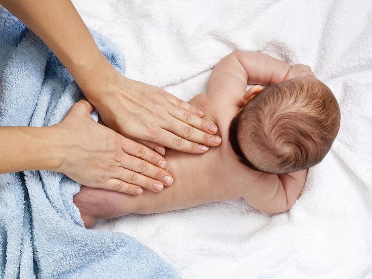 a baby laying on its back being massaged by someone's hands over a blue towel