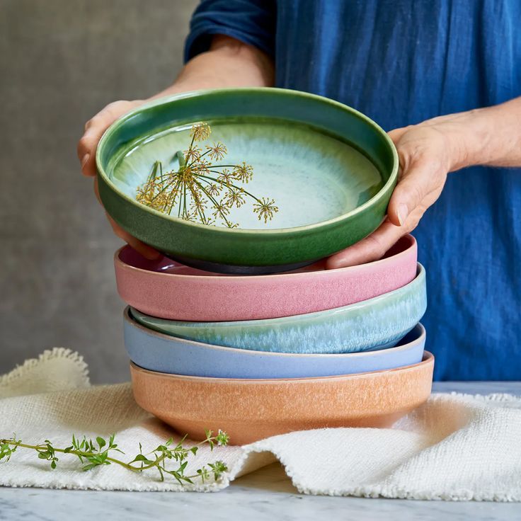 a person holding a stack of bowls with flowers in them on top of a table