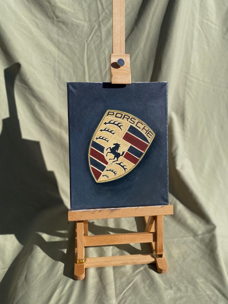 a small wooden easel with a painting on it's side and a porsche emblem painted on the front