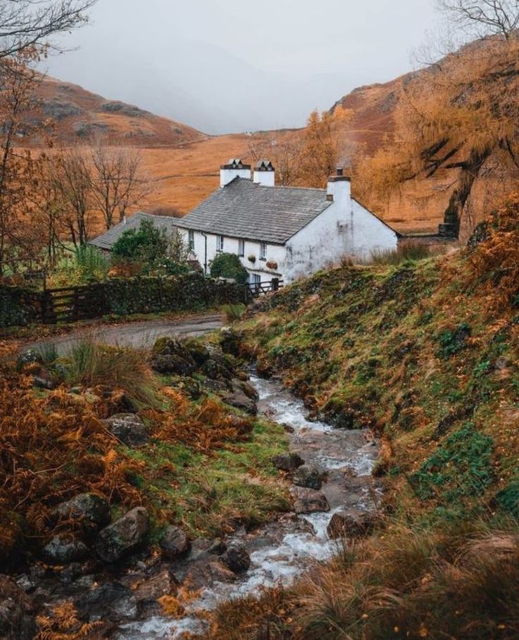 a small house sitting on the side of a hill next to a stream in front of it