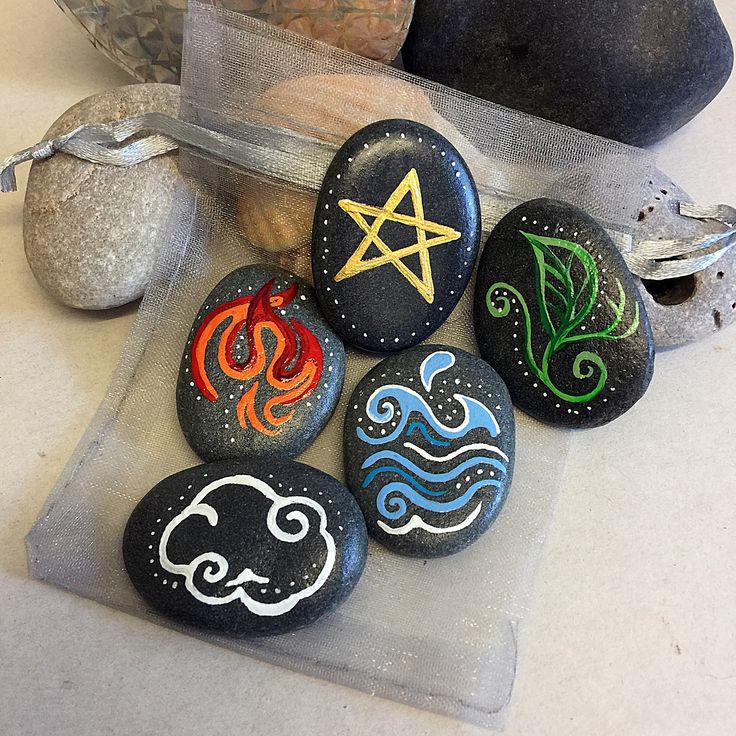 four painted rocks sitting on top of a table next to some stones with symbols drawn on them