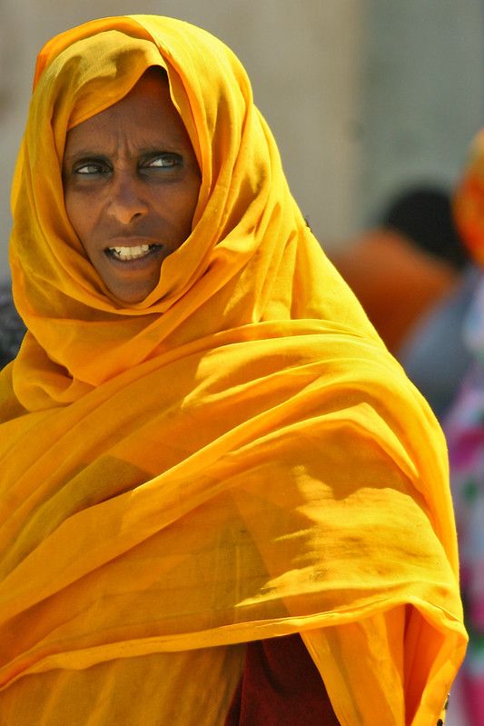 a woman wearing a yellow shawl and smiling at the camera with other people in the background