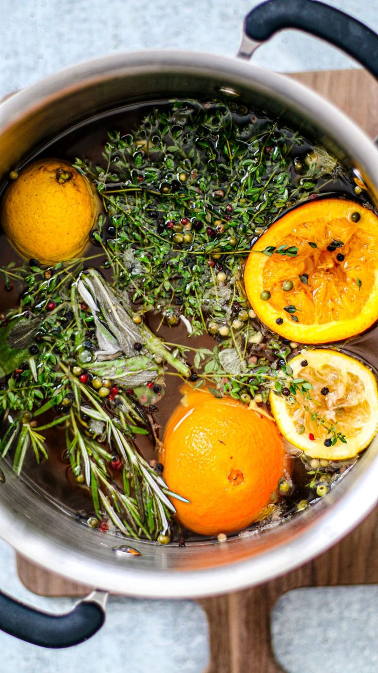 a pot filled with herbs and oranges on top of a wooden cutting board