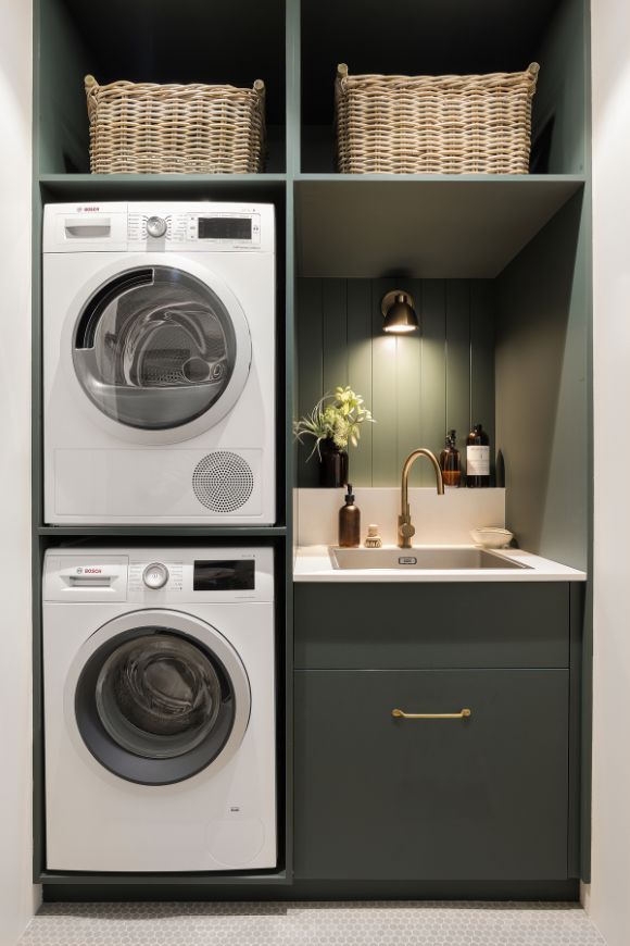 a washer and dryer in a laundry room with green cabinets, white counter tops and gold handles