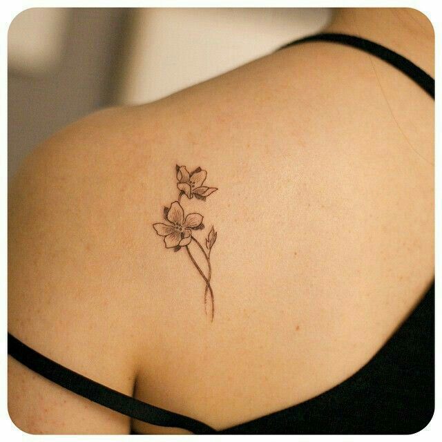 the back of a woman's shoulder with a small flower tattoo on her left side