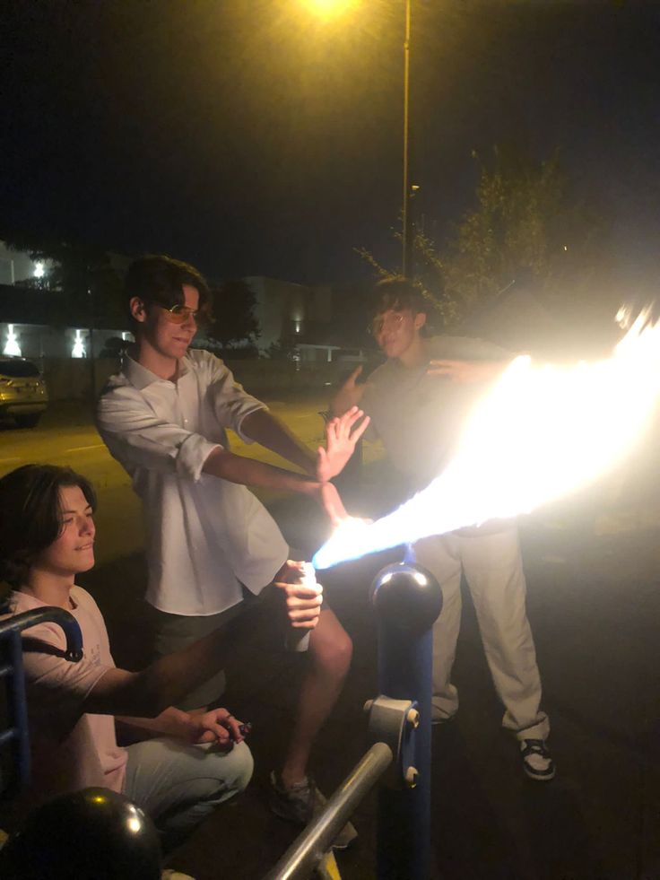 three people are sitting on the ground and one person is holding a lit sparkler