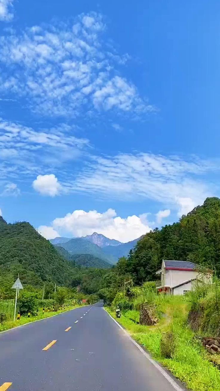 an empty road with mountains in the background and blue skies above it on a sunny day