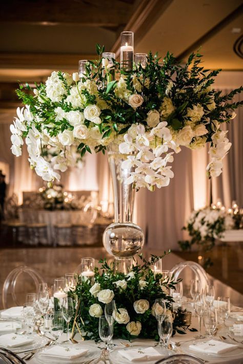 a tall vase filled with white flowers sitting on top of a table covered in candles