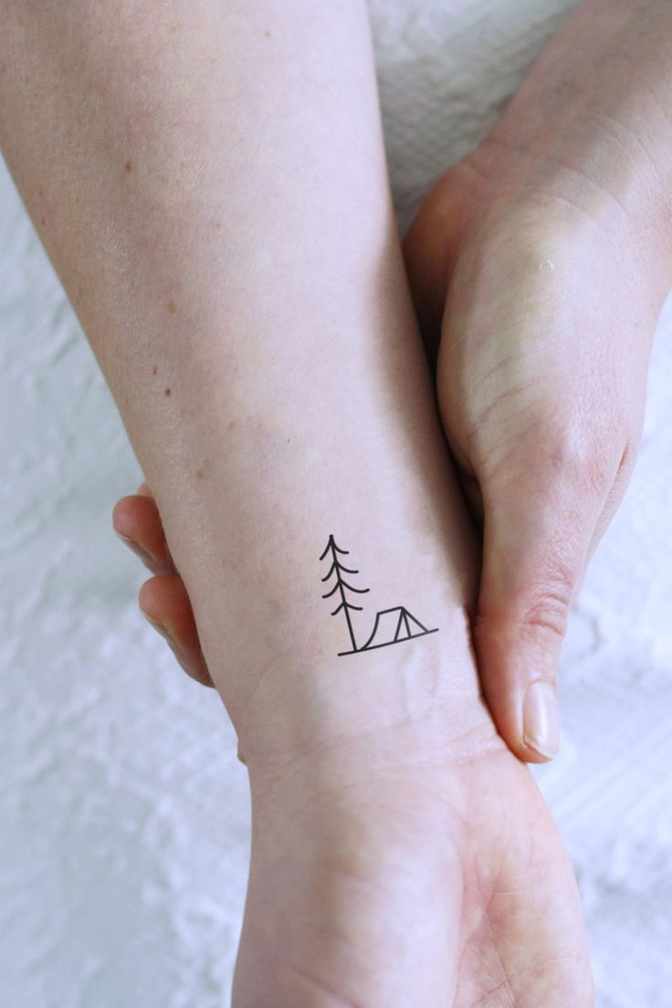 two hands holding each other with a small tattoo on the wrist that has a pine tree on it