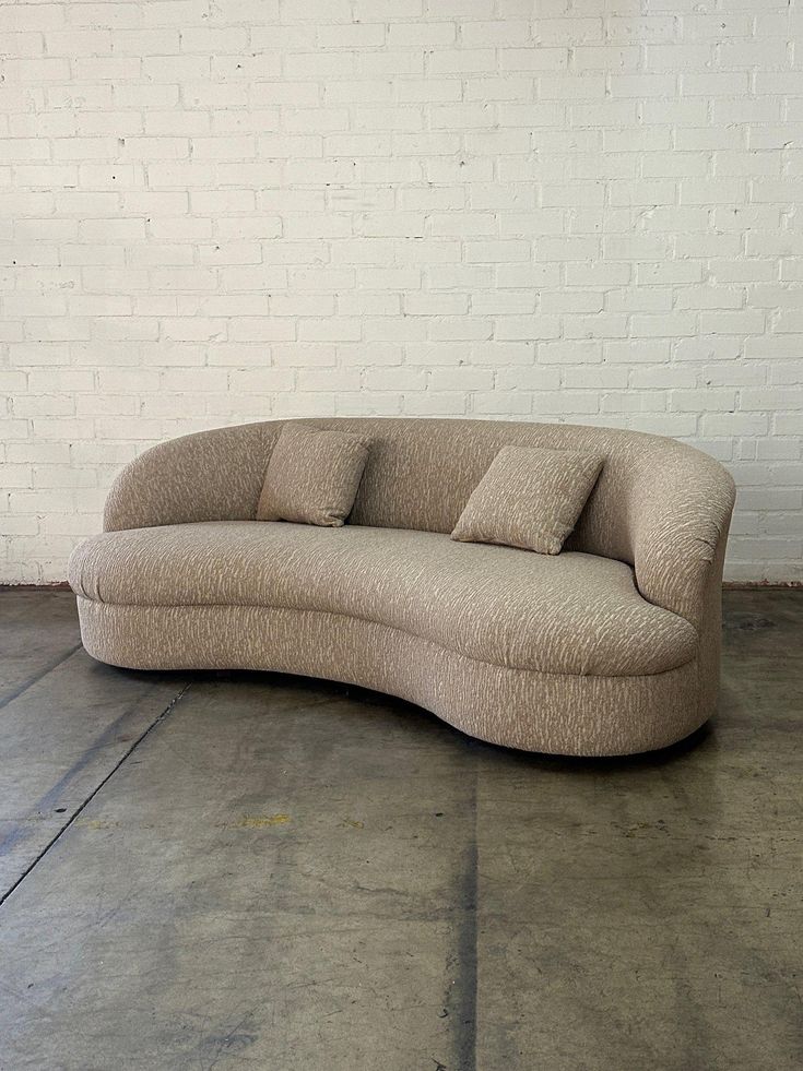 a curved couch sitting in front of a white brick wall