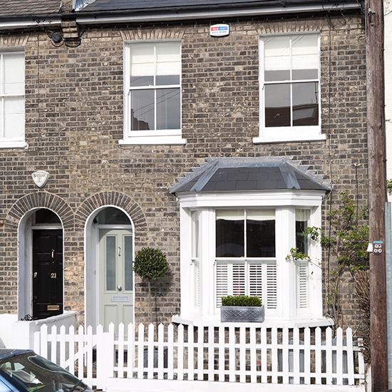 a car is parked in front of a brick house with white windows and shutters