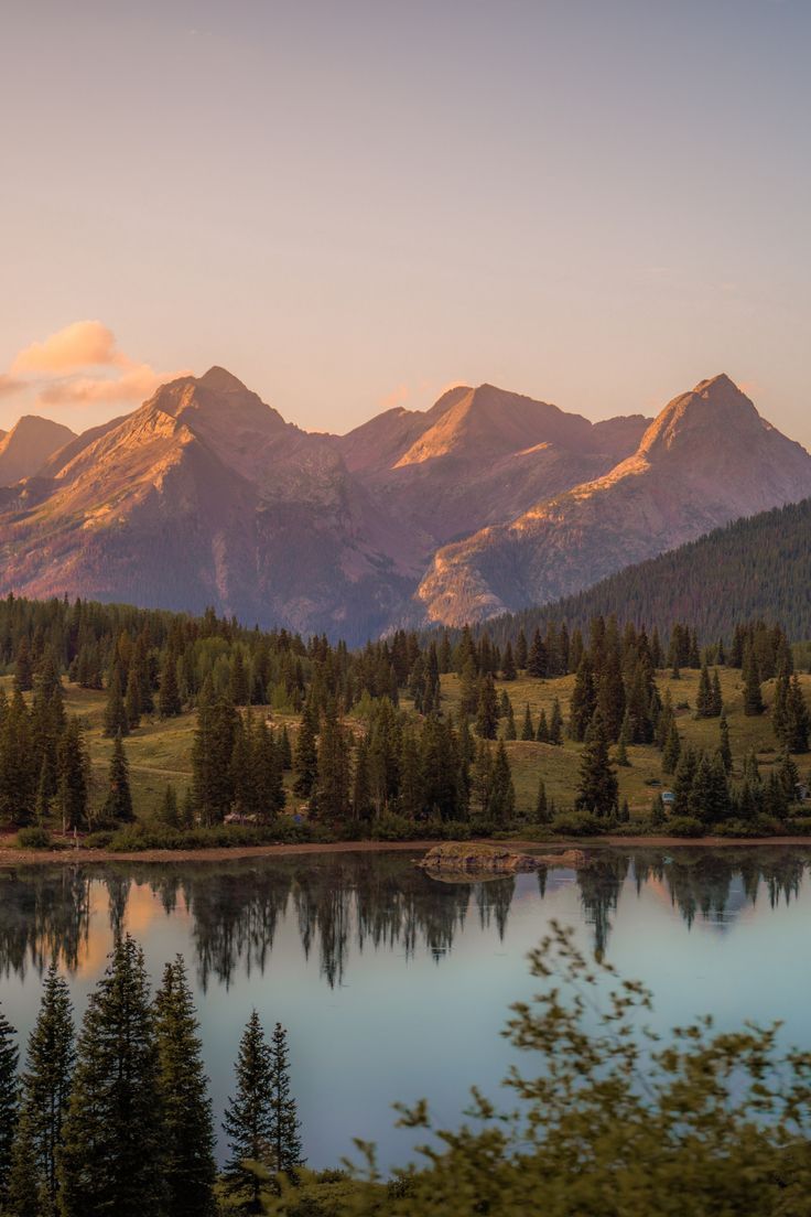 the mountains are reflected in the still water of this lake as the sun goes down