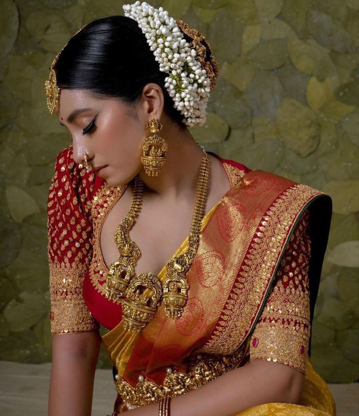 a woman in a red and gold sari sitting down with her hands on her knees