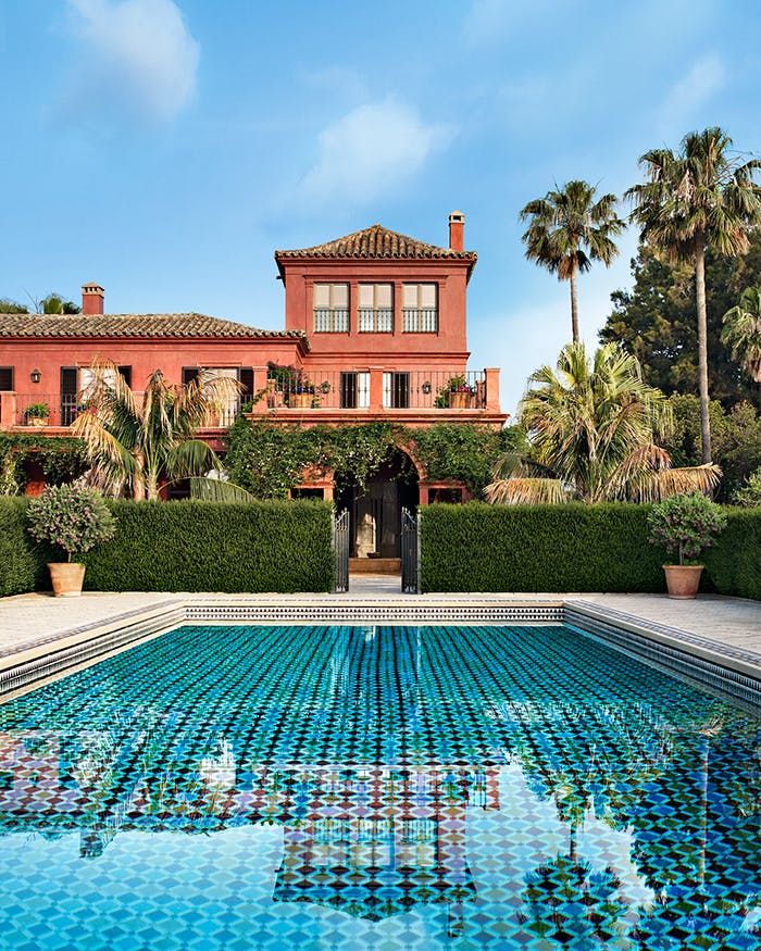 a large red house sitting next to a swimming pool in front of a palm tree