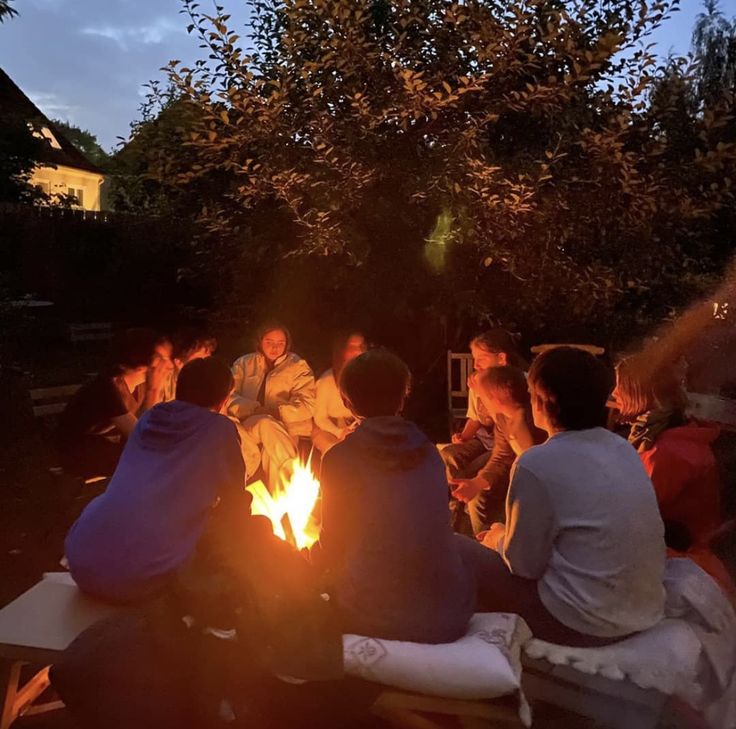 a group of people sitting around a campfire at night with their backs turned to the camera