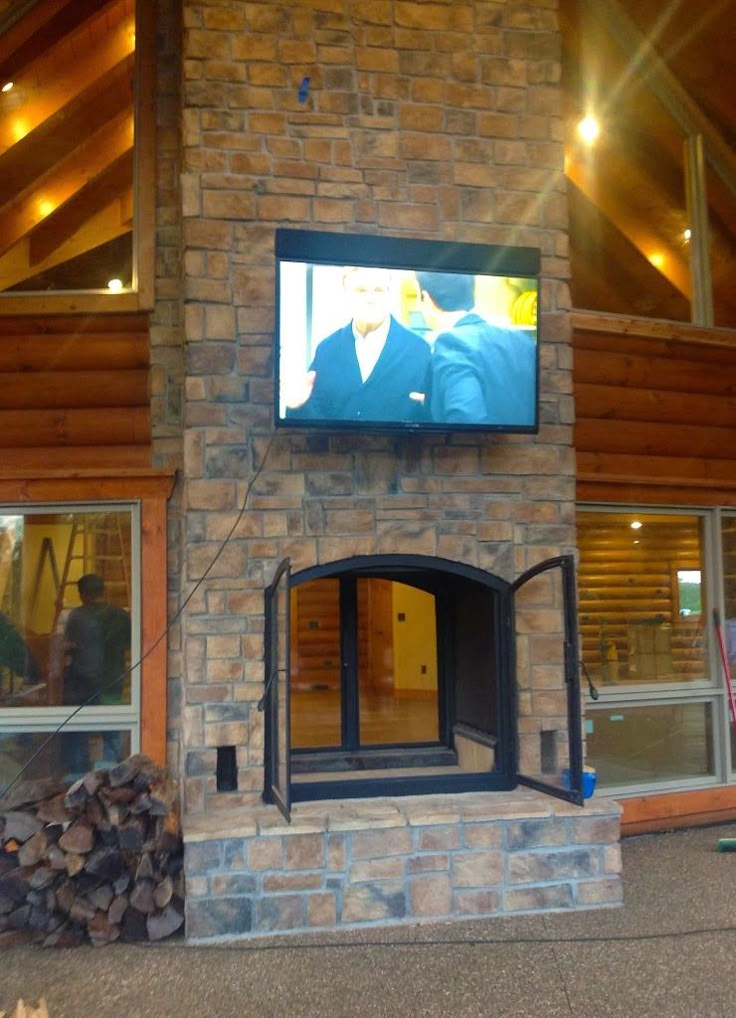 a large television mounted to the side of a stone fireplace in front of a building