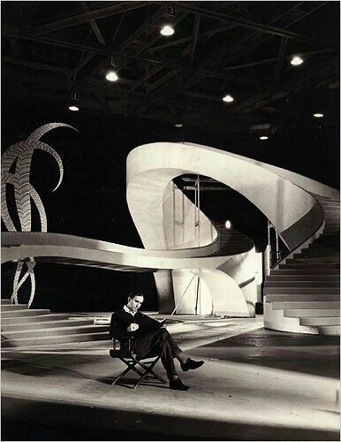 a man sitting in a chair on top of a stage next to an artistic sculpture