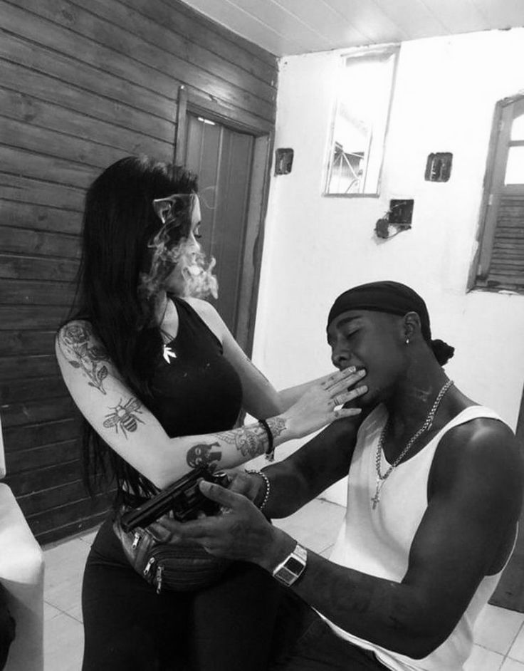 a woman is getting her makeup done by a man in a white tank top and black pants