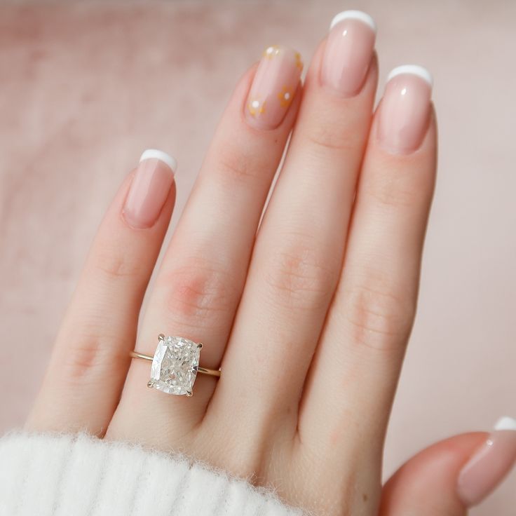 a woman's hand with french manies and an oval shaped diamond ring on it