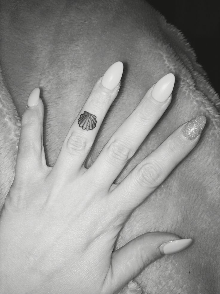 a woman's hand with a shell tattoo on her left ring and white nails