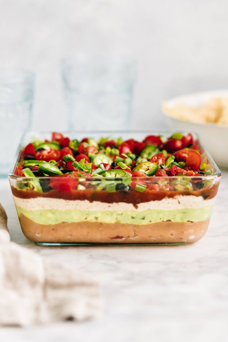 a glass dish filled with food sitting on top of a table next to a bowl of chips