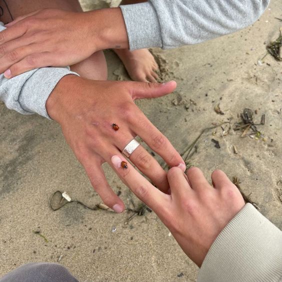 two people with their hands together on the beach, one is holding his wedding ring