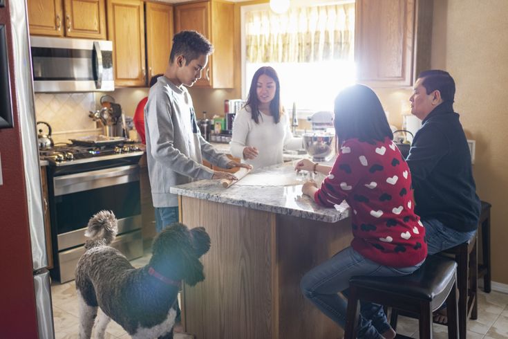 three people sitting at a kitchen counter with a dog