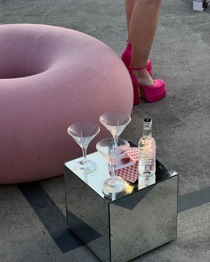 a mirrored table with wine glasses and bottles on it next to a pink bean bag