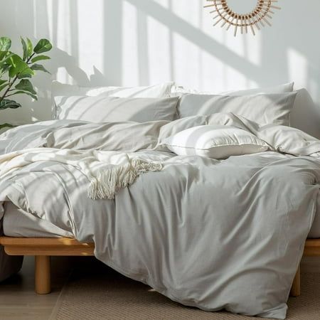 an unmade bed with white linens and pillows in a sunny room next to a potted plant