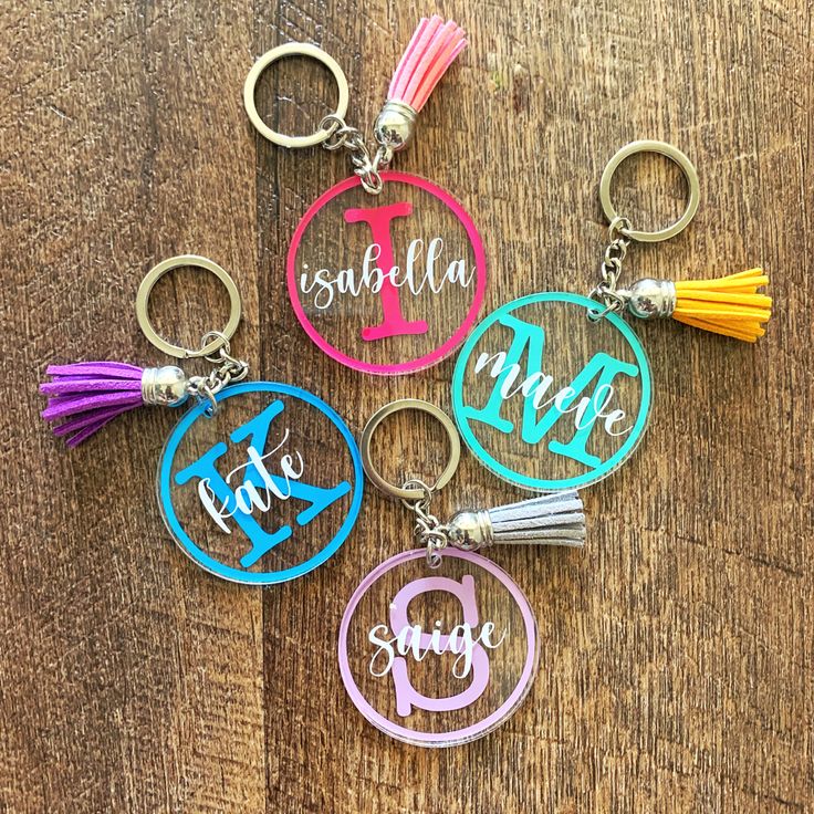 four personalized keychains with tassels on top of a wooden table