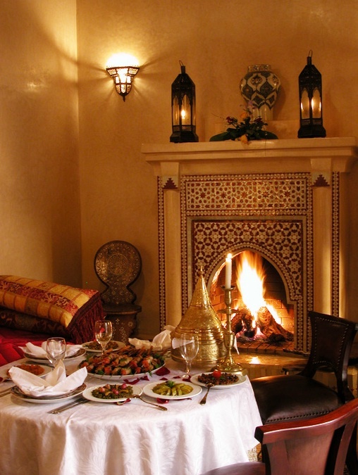 a table with food and wine in front of a fire place that is lit up