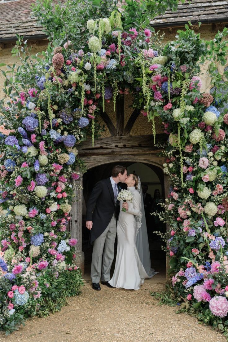 a bride and groom kissing in front of a flower covered archway at the end of their wedding day