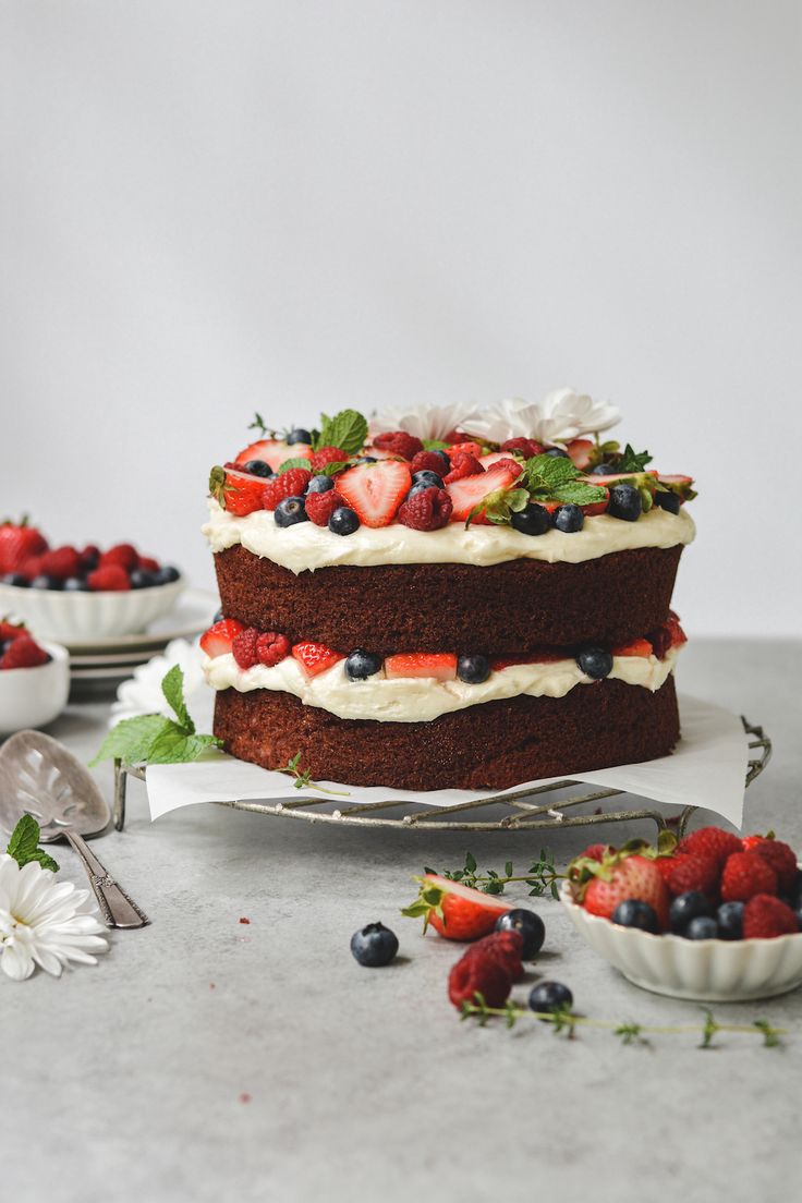 there is a cake with berries on it and two bowls of strawberries in the background