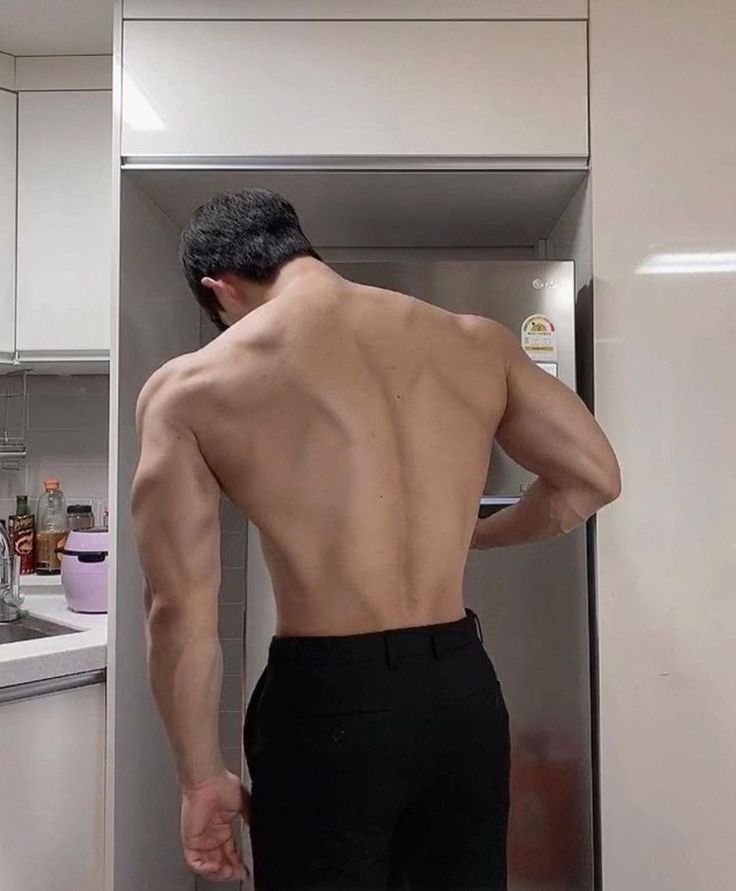 a shirtless man standing in front of a refrigerator freezer with his back to the camera