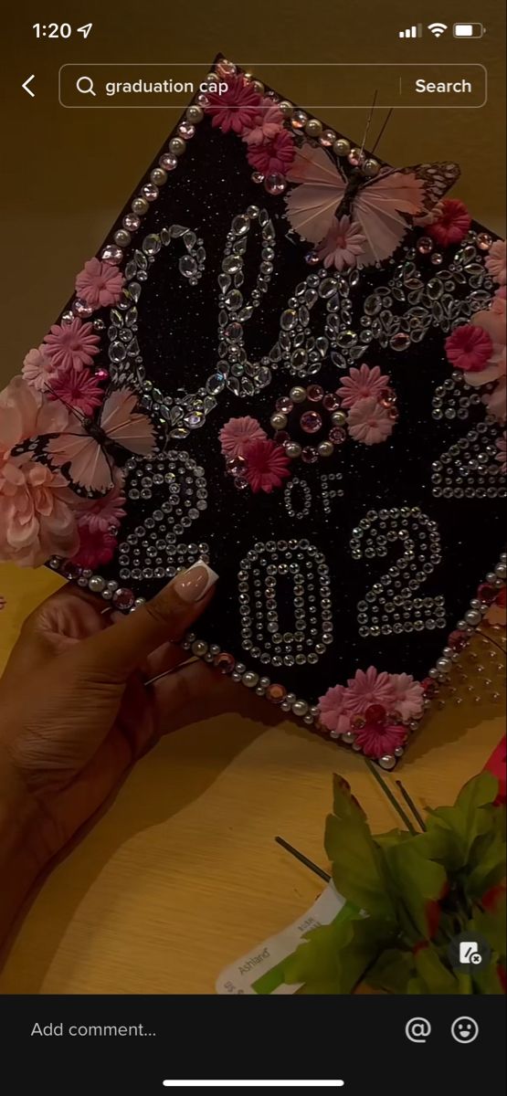 someone is holding up a graduation cap decorated with pink flowers and butterflies, which are on top of a table