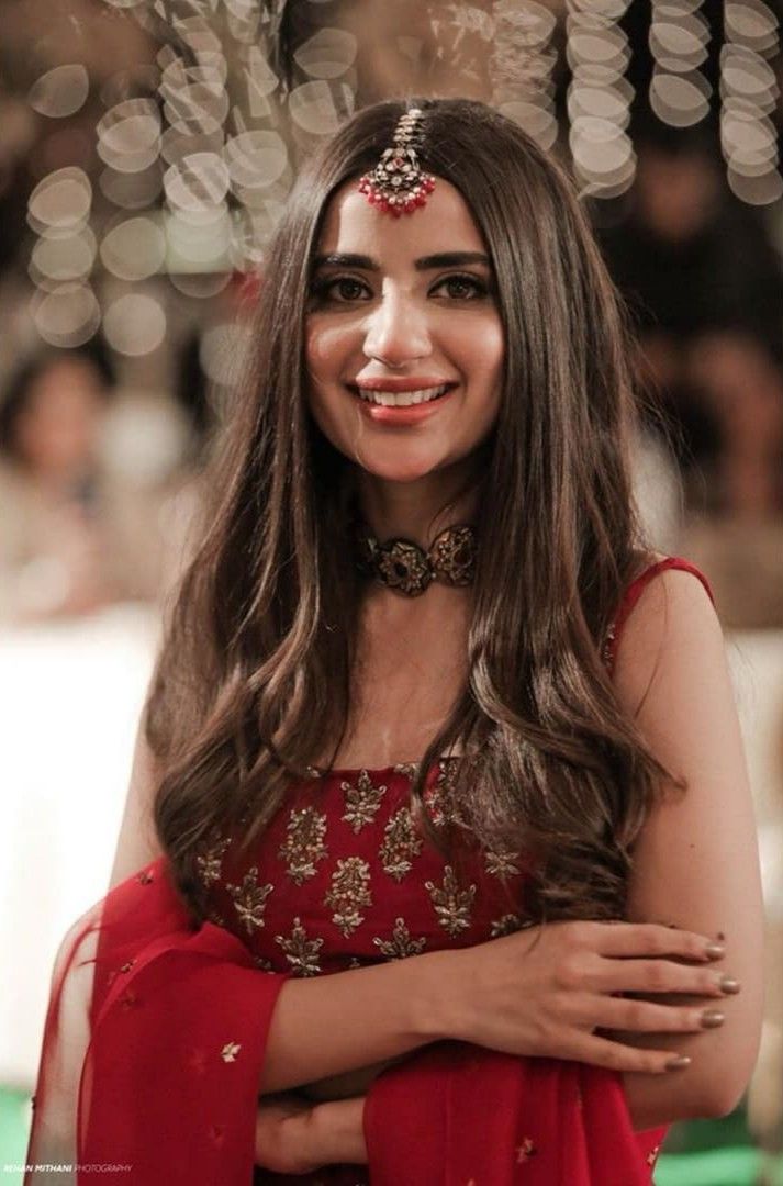 a woman with long brown hair wearing a red dress and smiling at the camera while holding her arms crossed