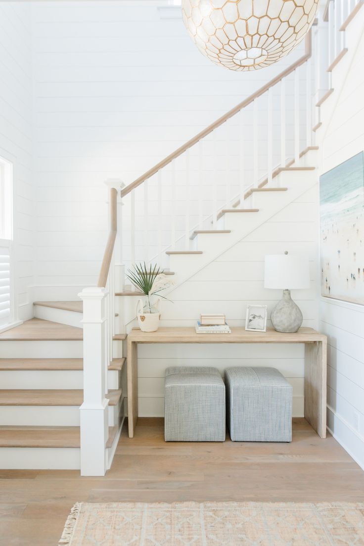 a white staircase with two stools next to it and a light fixture hanging from the ceiling