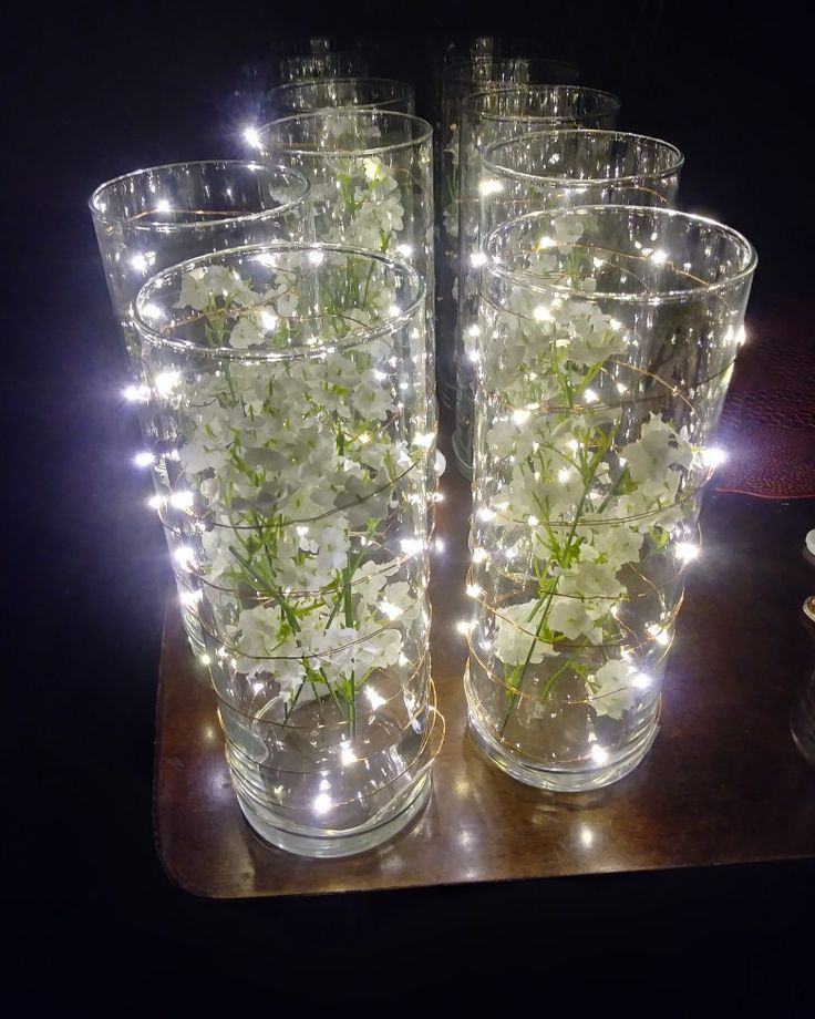 two clear vases with white flowers in them on a wooden table next to a mirror