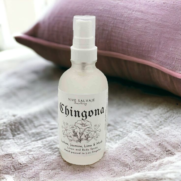 a close up of a bottle of liquid on a bed with a pillow in the background