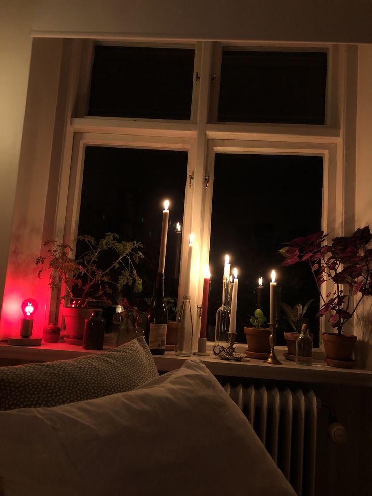 candles are lit in front of a window with potted plants on the windowsill