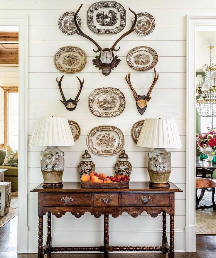 a table with two lamps and plates on it in front of a wall mounted deer head