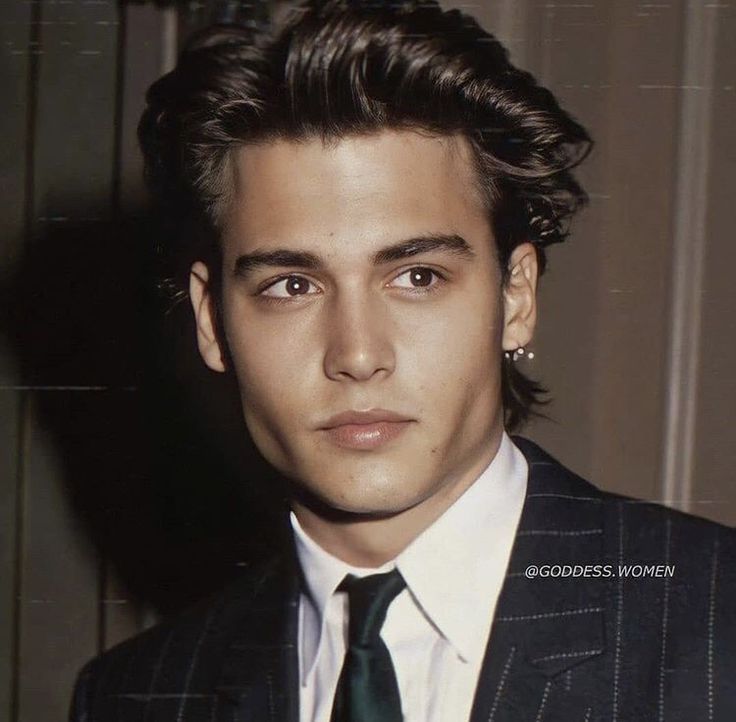 a young man in a suit and tie posing for a photo with his hair pulled back