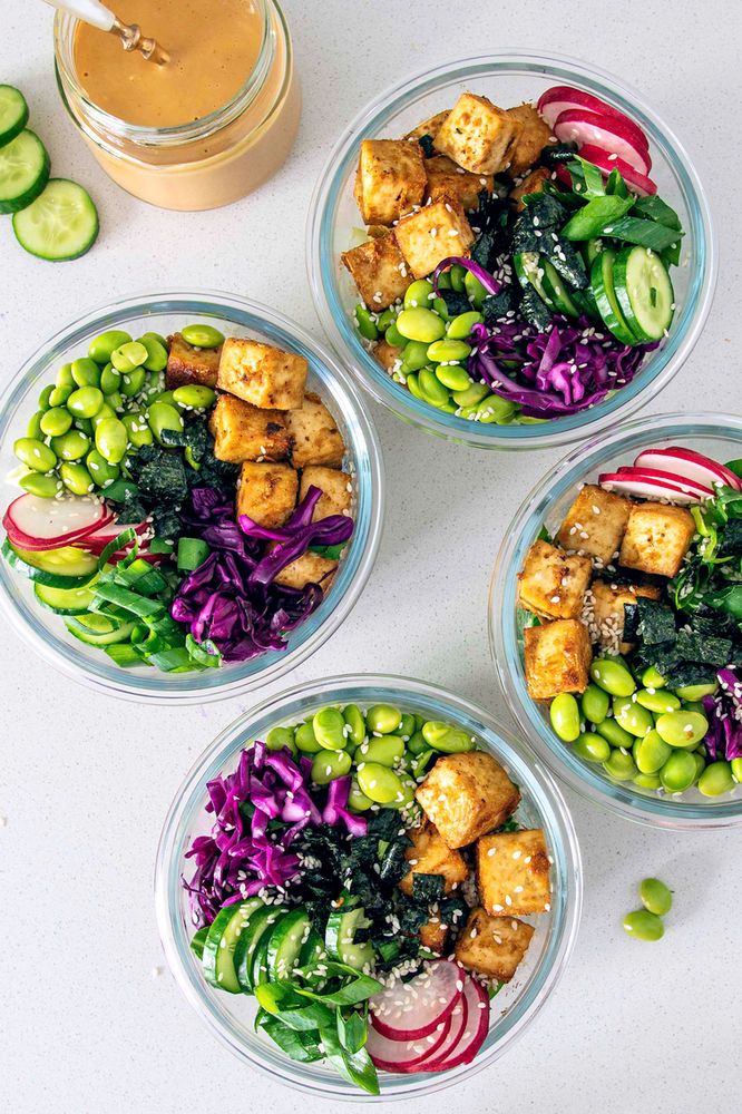 three bowls filled with vegetables and tofu on top of a white table next to cucumbers