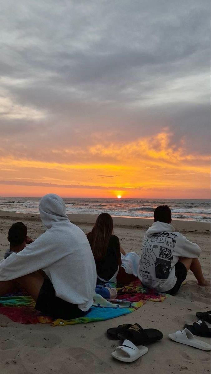 three people sitting on the beach watching the sun set