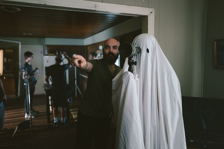 a man dressed as a ghost pointing at something in front of him and people standing around