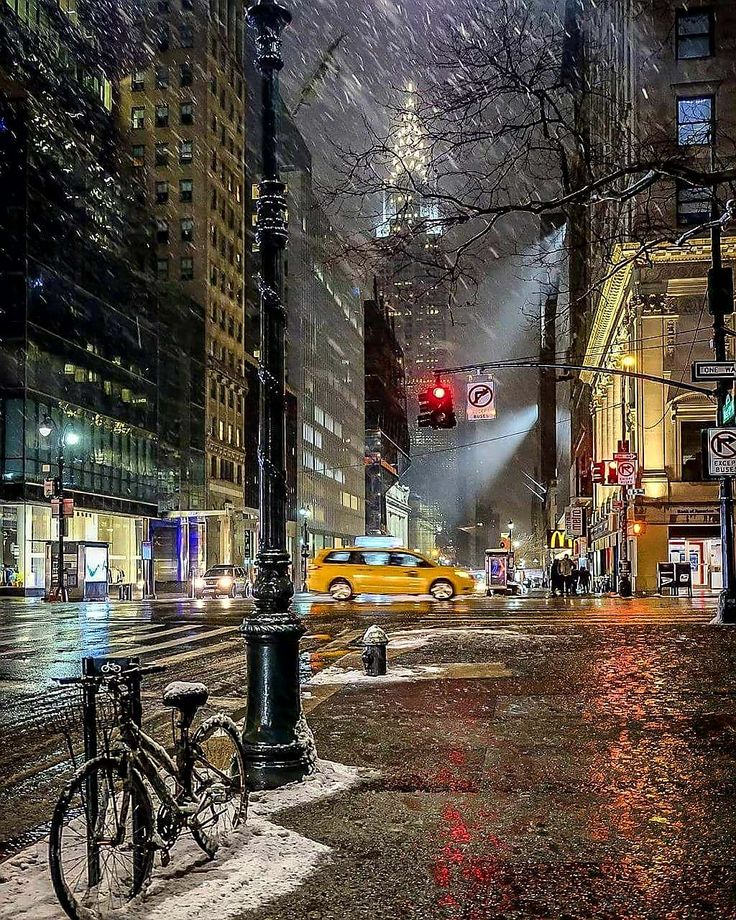 a city street filled with lots of traffic next to tall buildings covered in snow at night