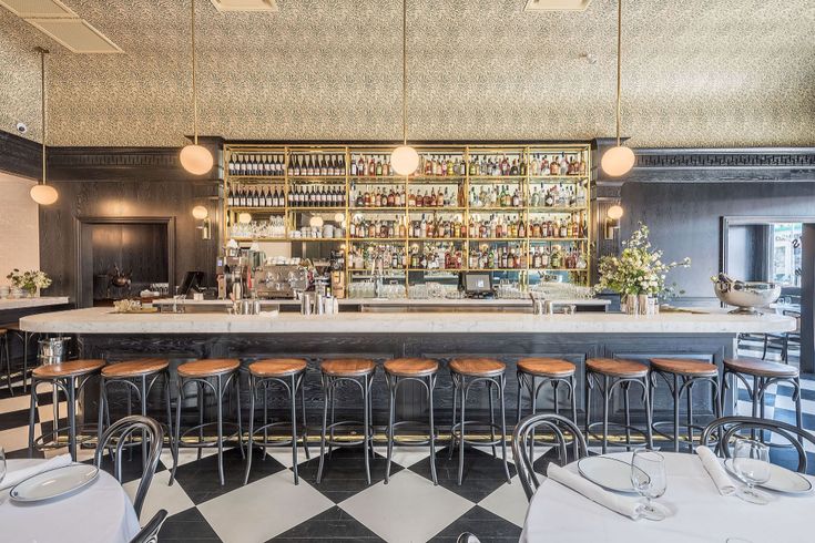 an empty restaurant with tables and stools in front of the bar, filled with liquor bottles