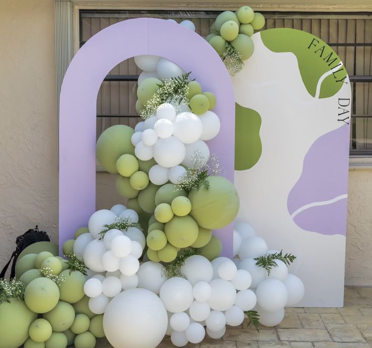 balloons and greenery are arranged in front of the entrance to an outdoor space that is decorated with purple, white and green